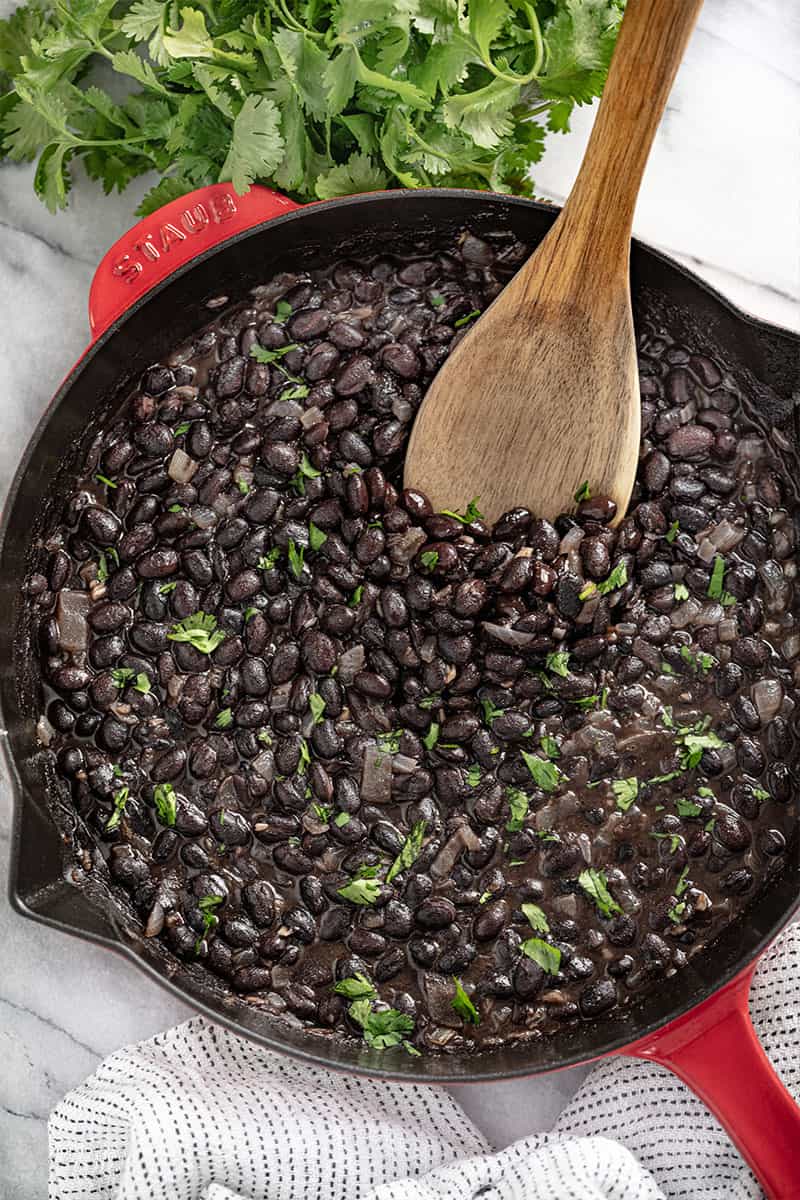 Bird's eye view of Mexican Black Beans in a cast-iron skillet with a wooden spoon in it.