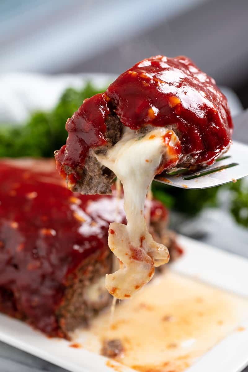 Slice of Mozzarella Stuffed Meatloaf with cheese oozing out of it being held up by a spatula.