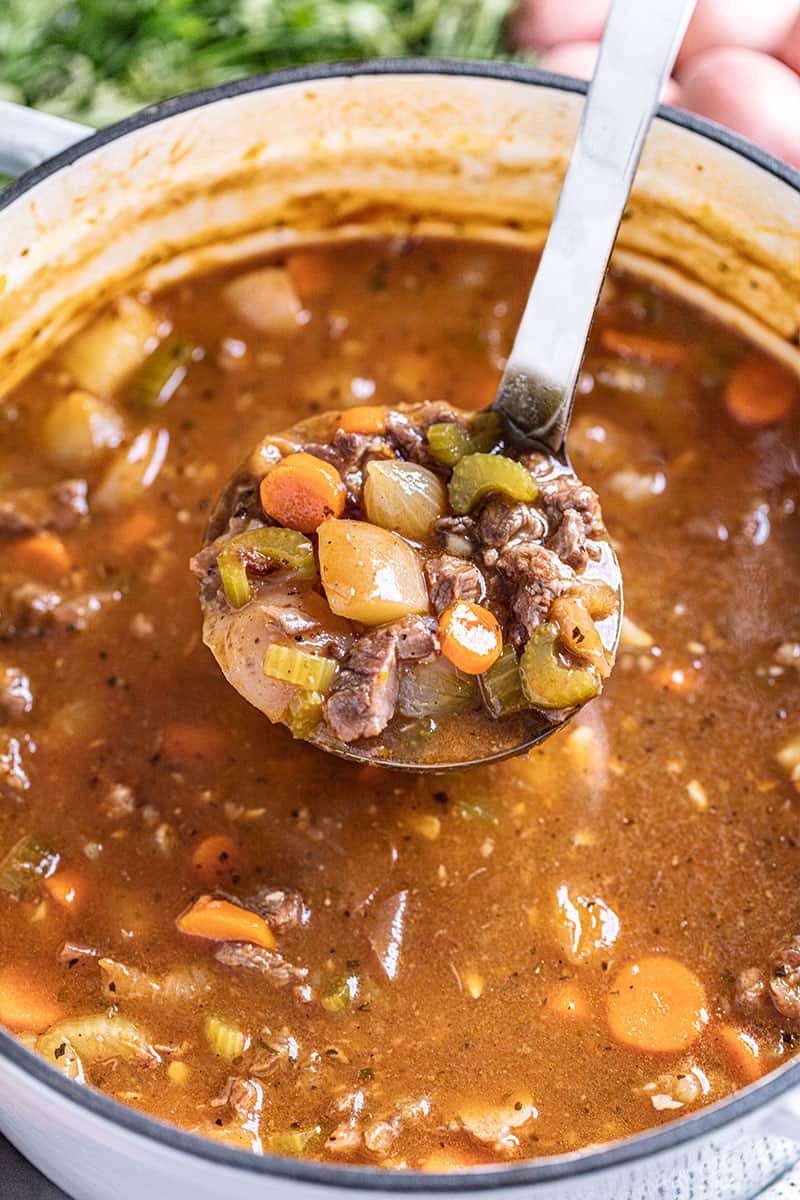 Bird's eye view of a ladle full of beef Stew above the pot.