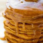 A stack of pumpkin pancakes covered in syrup with a pat of butter on top.