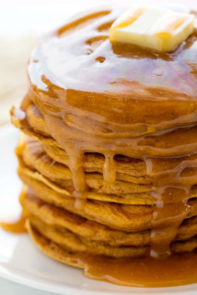 A stack of pumpkin pancakes covered in syrup with a pat of butter on top. 