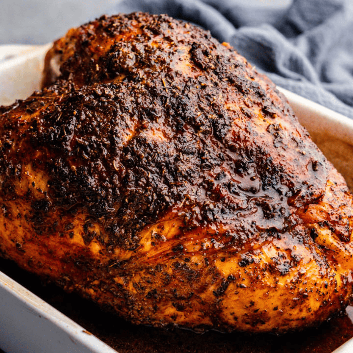 A close up view of a roasted turkey breast seasoned with cajun spices in a white roasting pan.