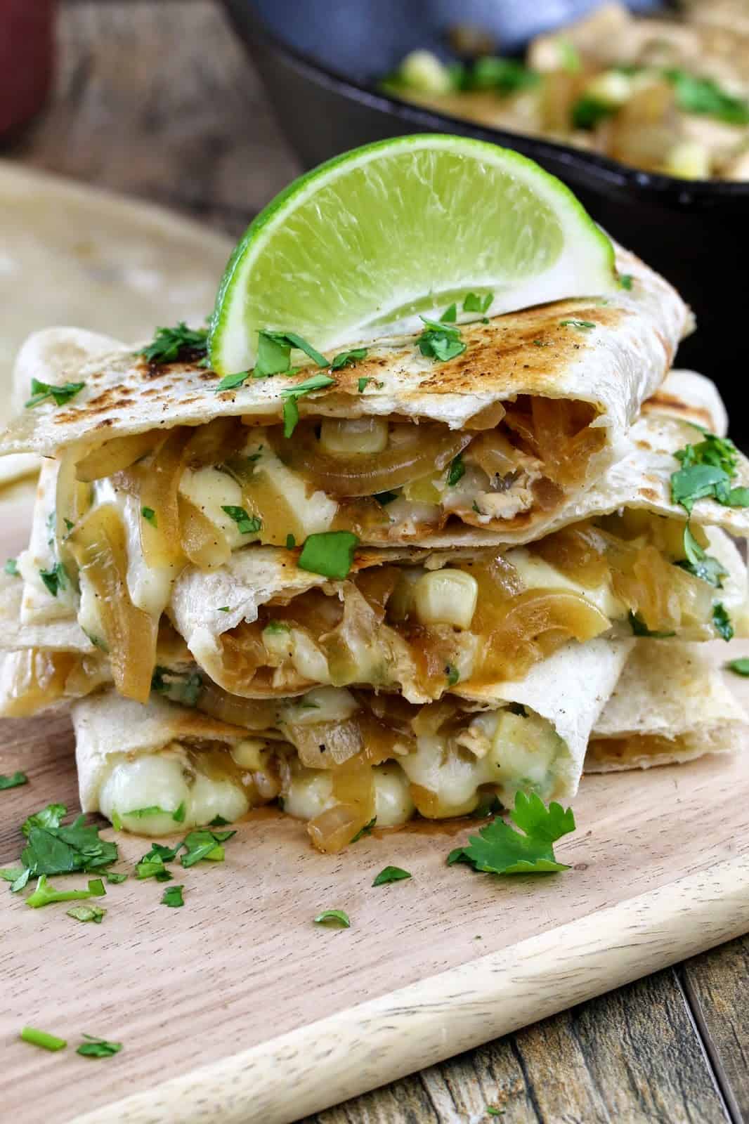 Close up of A stack of quesadillas spilling over with cheese, onions, corn and chicken and garnished with fresh cilantro and a lime wedge