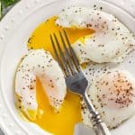 A plate of poached eggs seasoned with salt and pepper. Yolks are cut into with a fork and runny