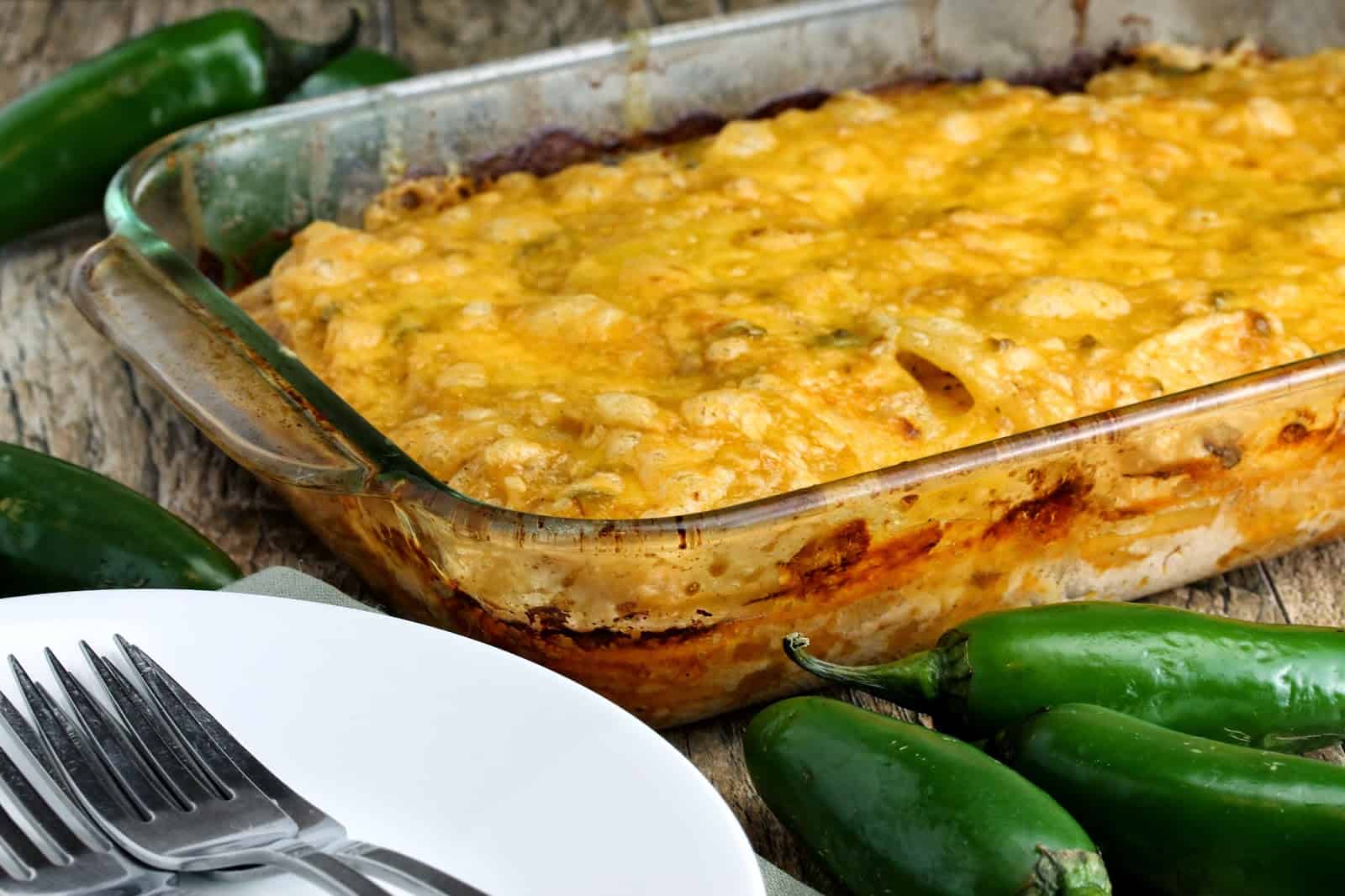 Jalapeno scalloped potatoes in a glass baking dish next to some plates and forks.