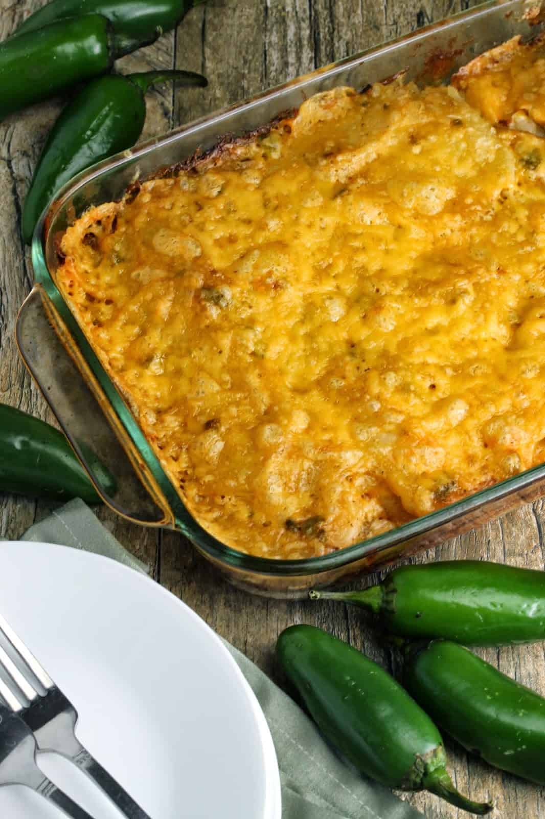 Bird's eye view of jalapeno scalloped potatoes in a glass baking dish next to a stack of plates and forks.