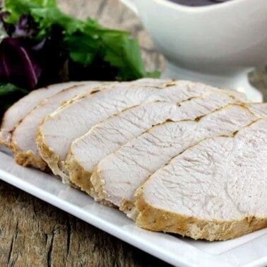 Slices of roasted turkey on a white plate with a green salad in the background