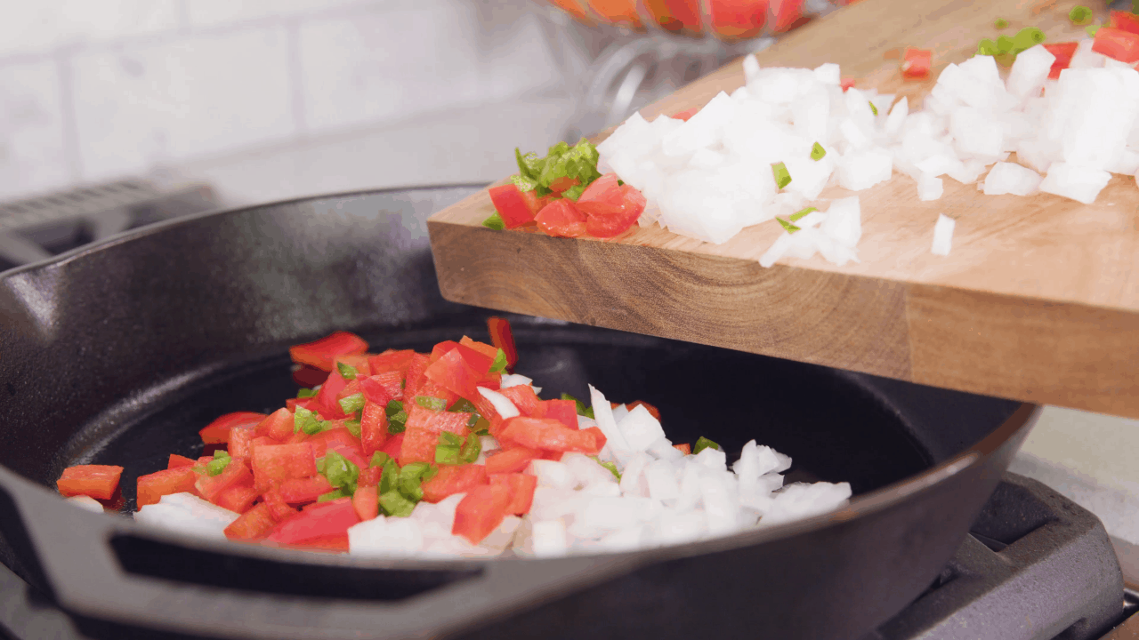 Shakshuka Vegetables being placed into a cast-iron skillet.