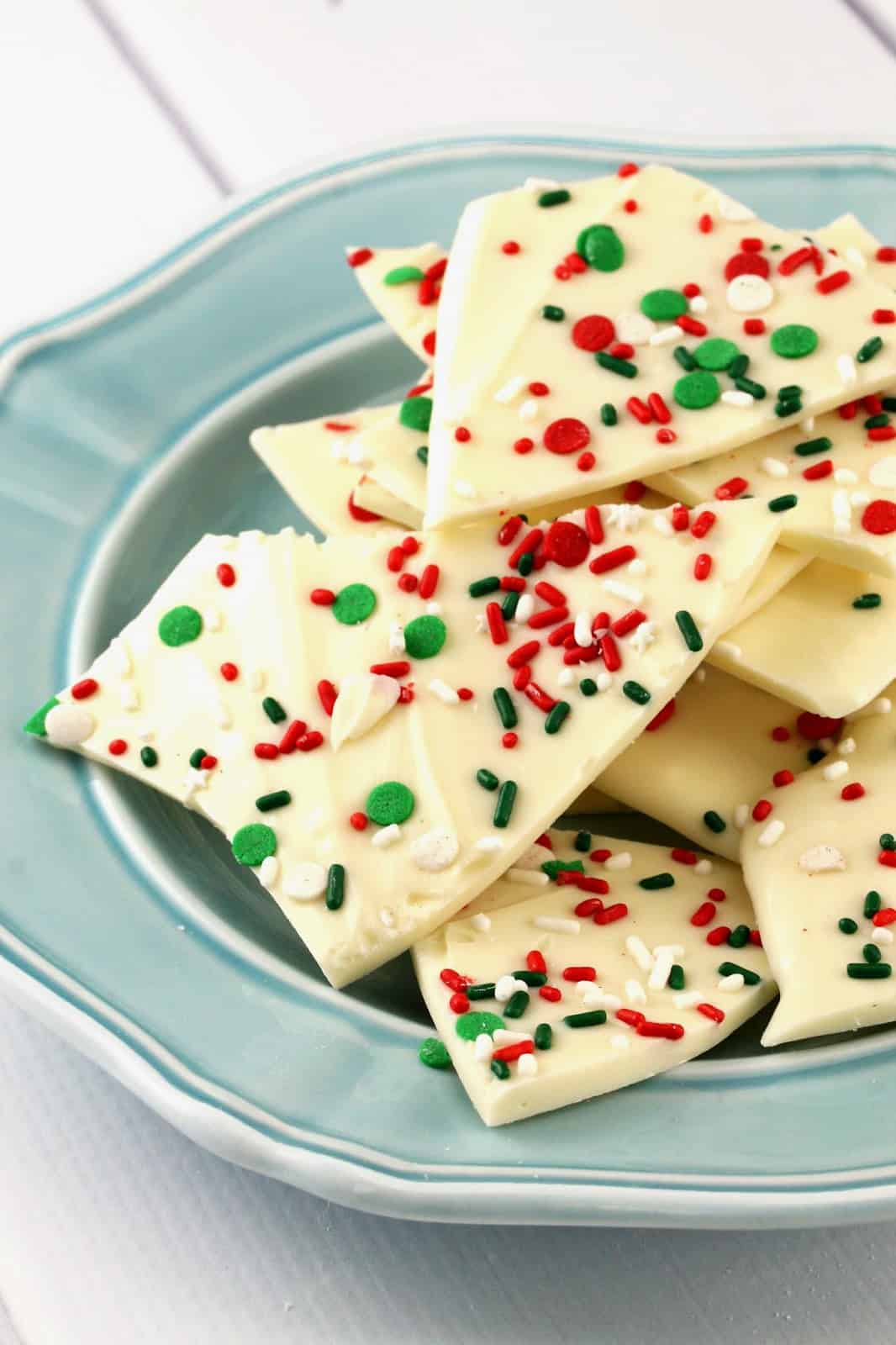 White Chocolate Christmas Sprinkle Bark stacked on a plate is sprinkled with festive colors for a fun and easy to make treat