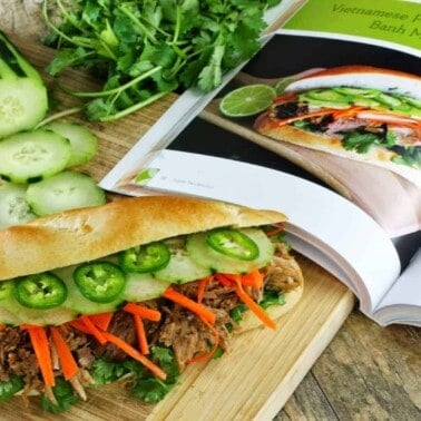 Slow Cooker Vietnamese Banh Mi Sandwich on a cutting board sitting next to a an open cookbook