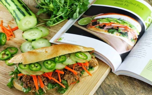 Slow Cooker Vietnamese Banh Mi Sandwich on a cutting board sitting next to a an open cookbook