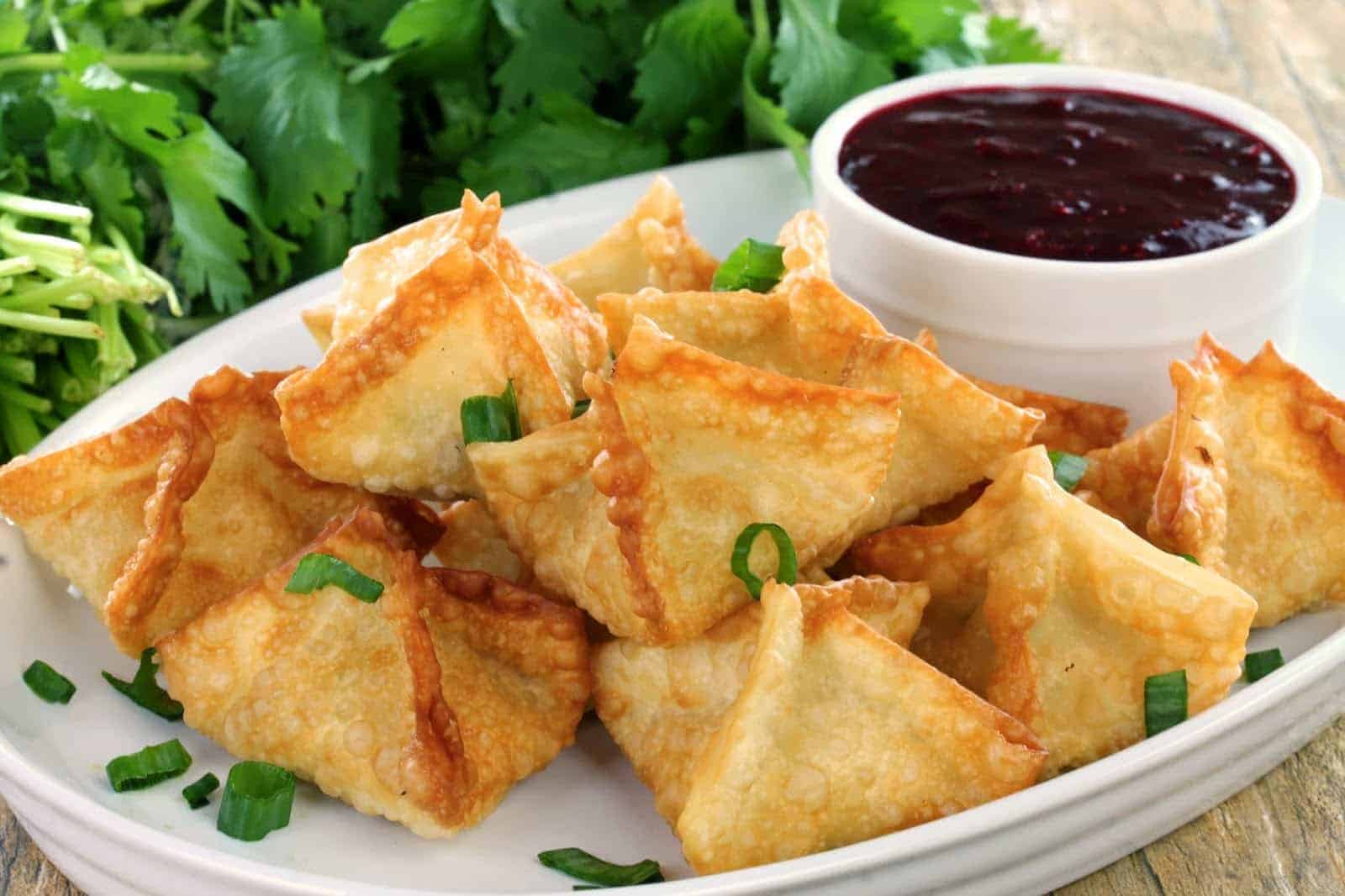 Crab Rangoons on a white plate with a dipping sauce.