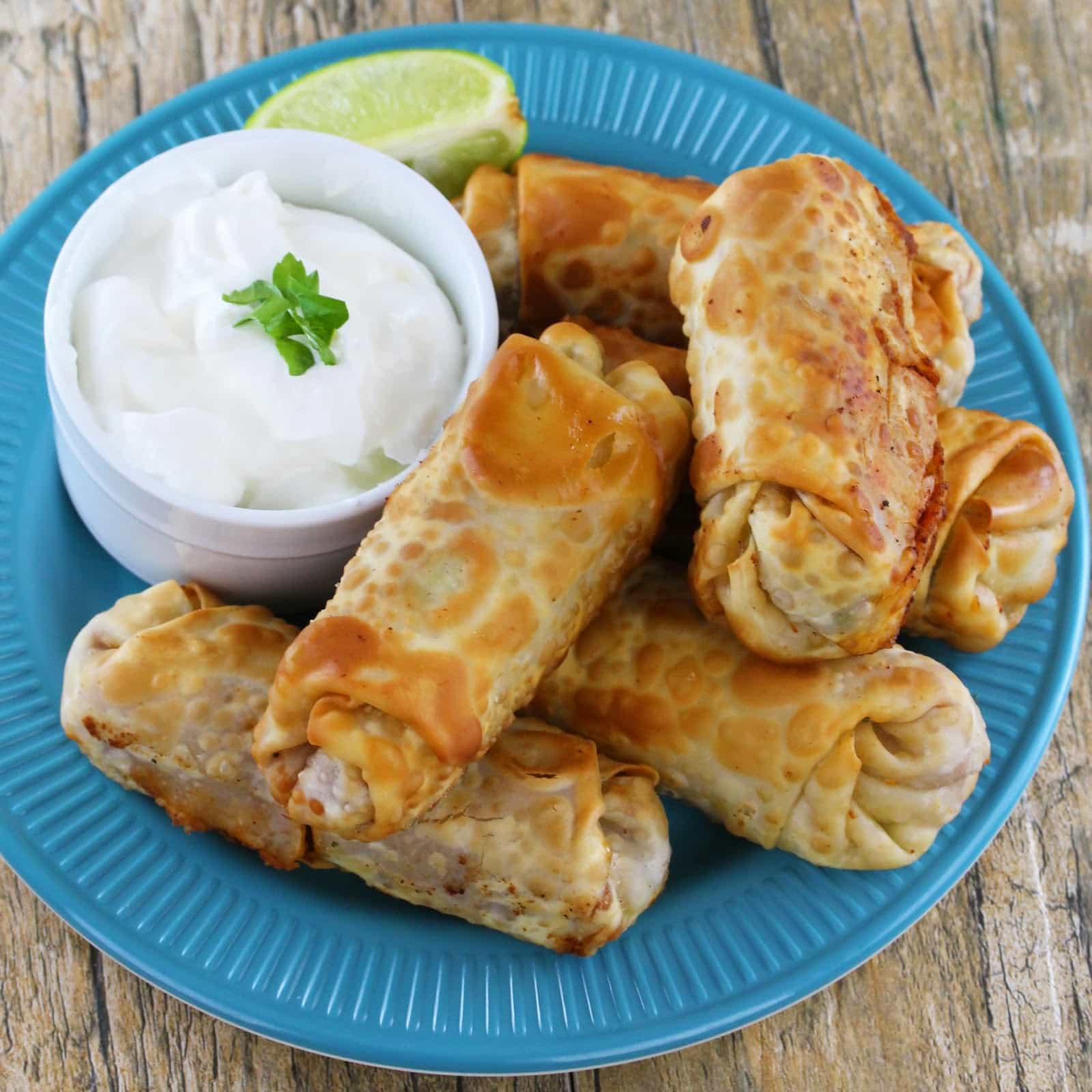 A stack of Mexican egg rolls on a blue plate with a side of sour cream