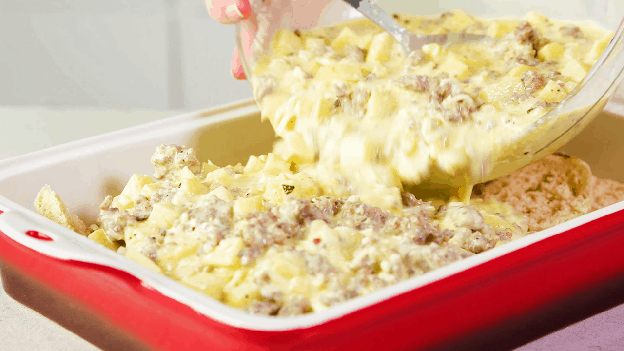 Pouring egg and sausage mixture over english muffins in a 9x13 pan
