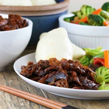 Slow cooker shinese bbq pork on a white plate with veggies and rolls.
