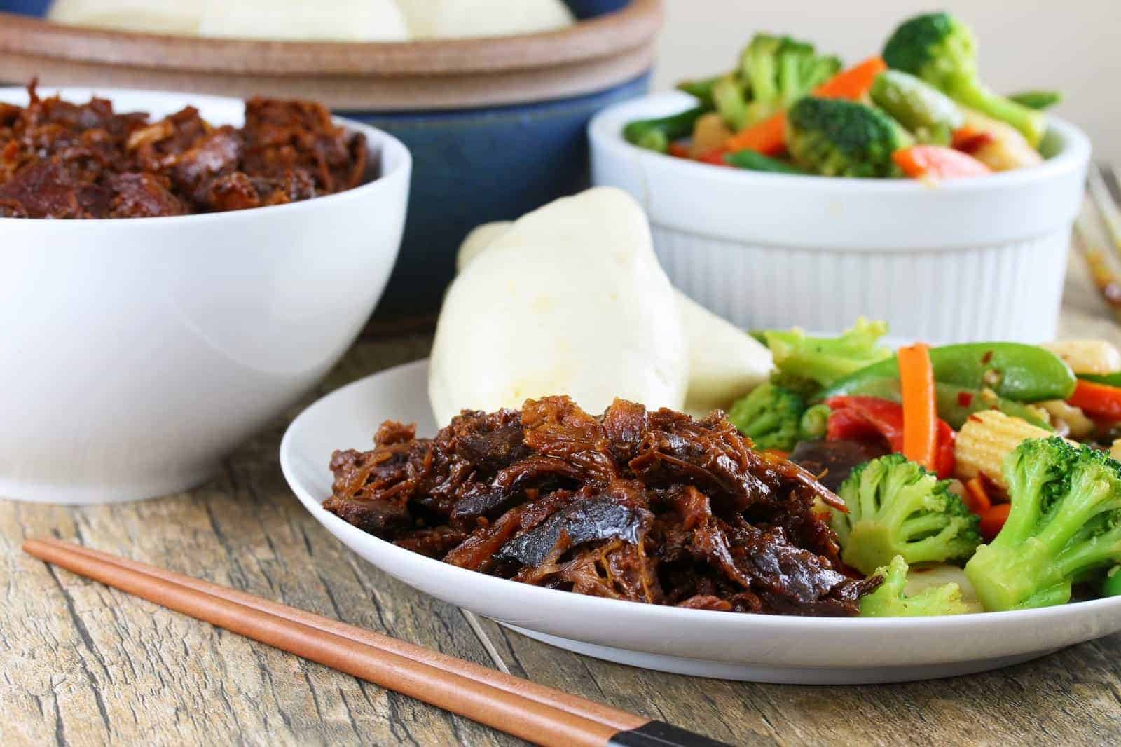 Slow cooker shinese bbq pork on a white plate with veggies and rolls.
