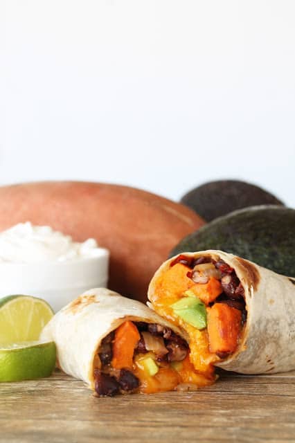 A sweet potato burrito cut in half with the insides oozing out on a counter top.