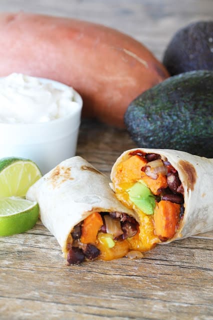 Angled view of a sweet potato burrito cut in half with the insides oozing out on a counter top.