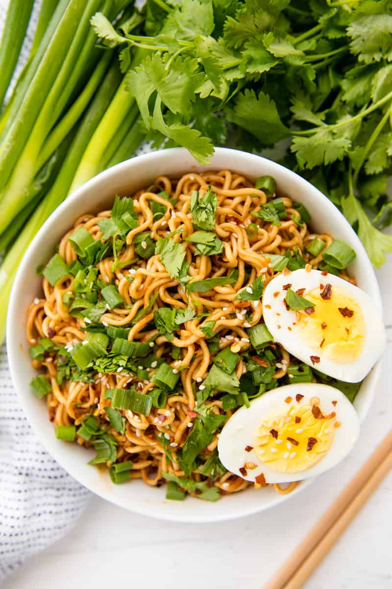 Overhead view of a bowl of sriracha ramen noodles with green onions and a boiled egg on top