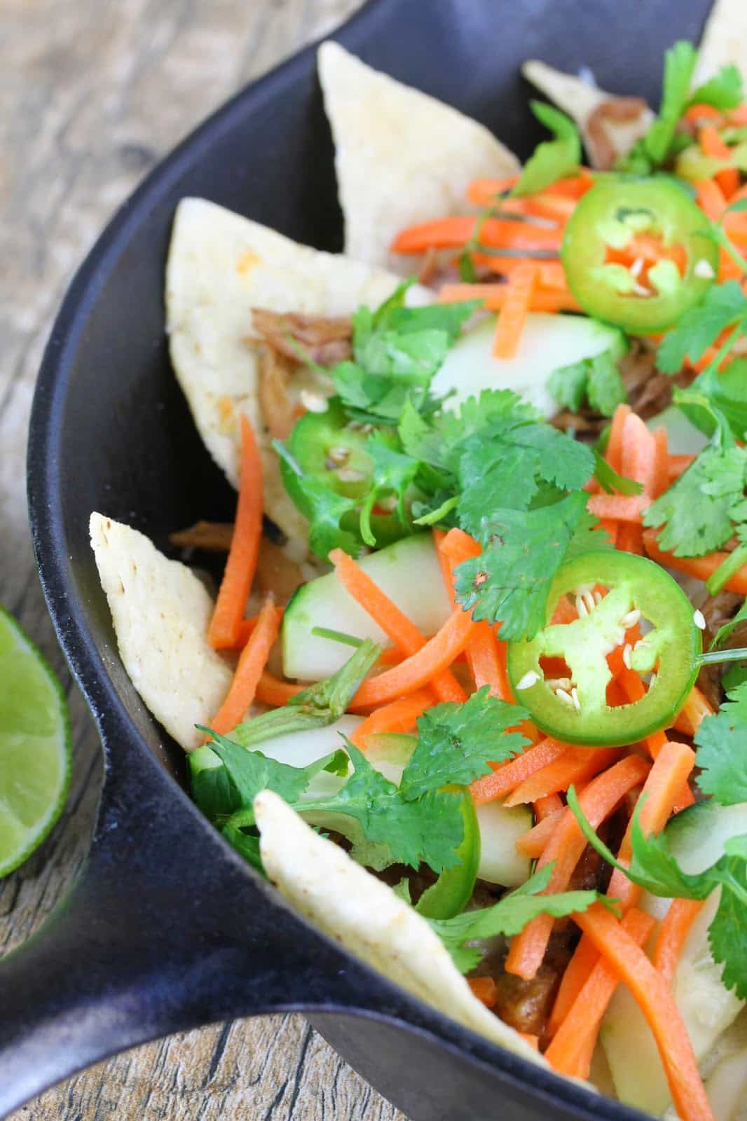 Bahn mi nachos in a skillet with slow cooker pork, carrots, cucumber, jalapeno and garnished with cilantro