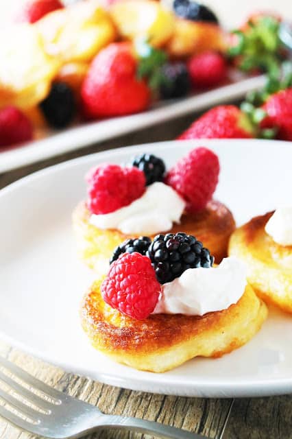 Three fried pancakes on a white plate topped with whipped cream and berries.