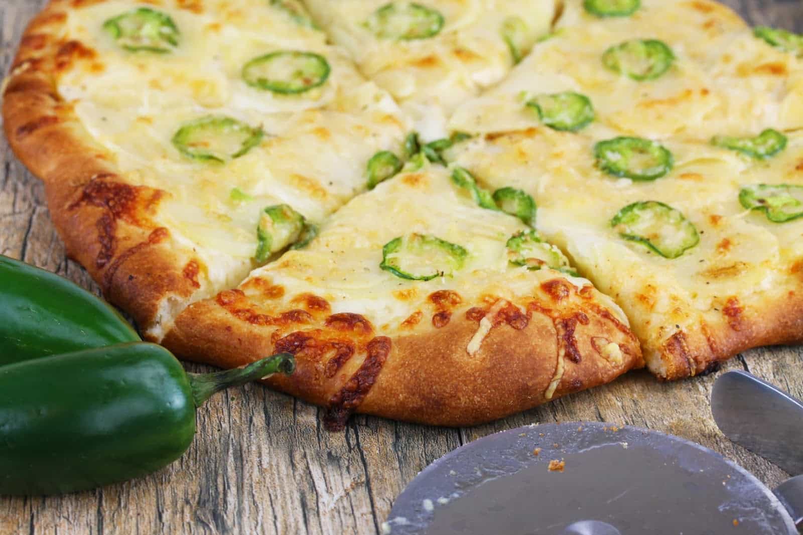 Jalapeno Scalloped Potato Pizza fresh out of the oven, cut into slices with a pizza cutter