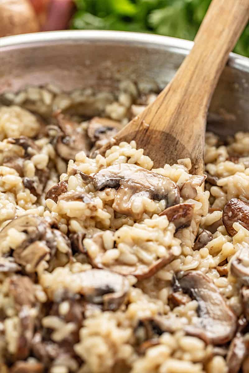 Close up Mushroom Risotto in a skillet with a wooden spoon in it.