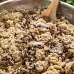 Close up Mushroom Risotto in a skillet with a wooden spoon in it.