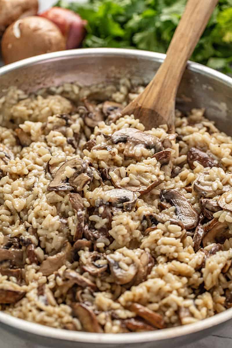 Close up Mushroom Risotto in a skillet with a wooden spoon in it.