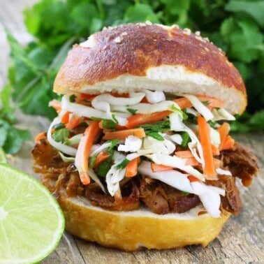Pulled pork sandwich on a white plate topped with a Thai Slaw on a white plate