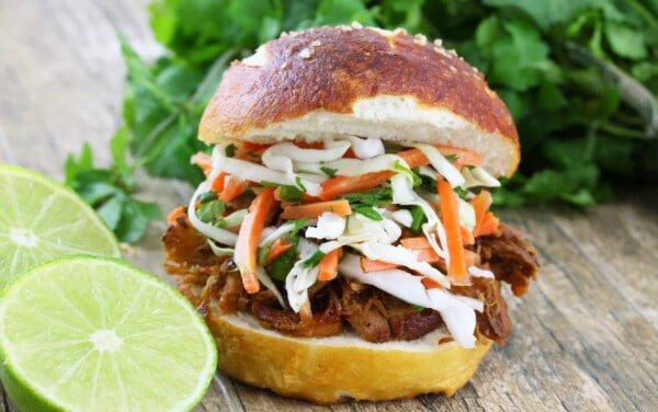 Pulled pork sandwich on a white plate topped with a Thai Slaw on a white plate