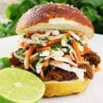 Pulled pork sandwich on a white plate topped with a Thai Slaw on a white plate