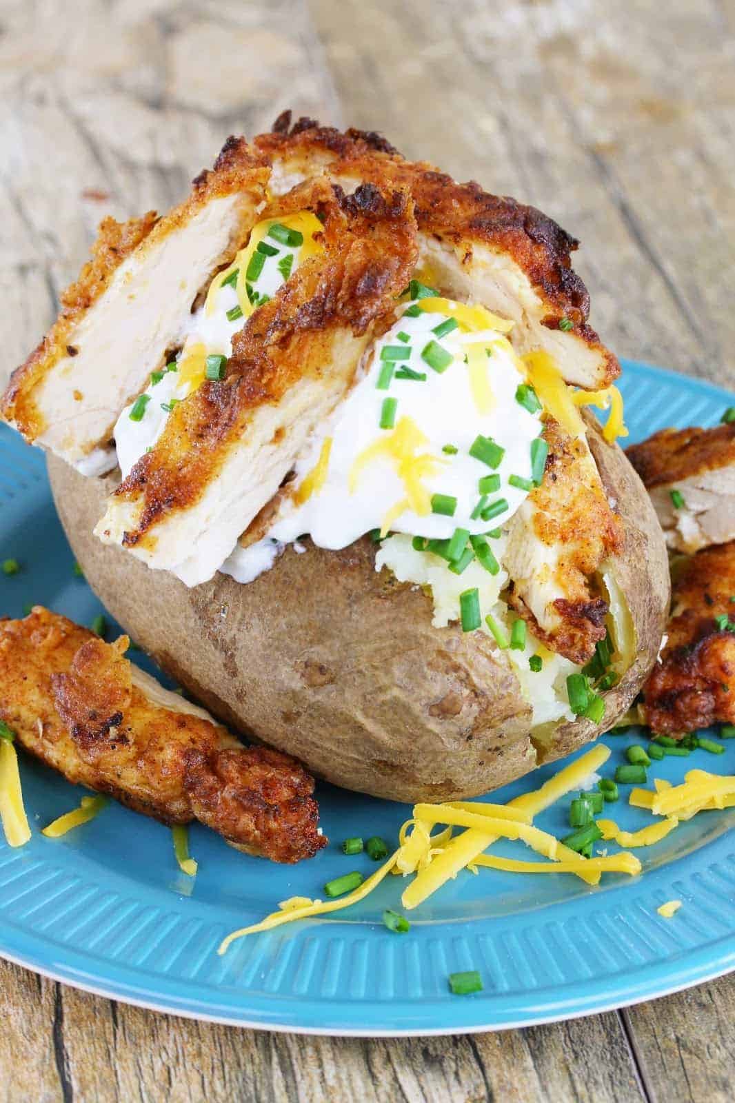 A baked potato stuffed with sour cream, cheddar cheese and fried chicken, garnished with fresh chives