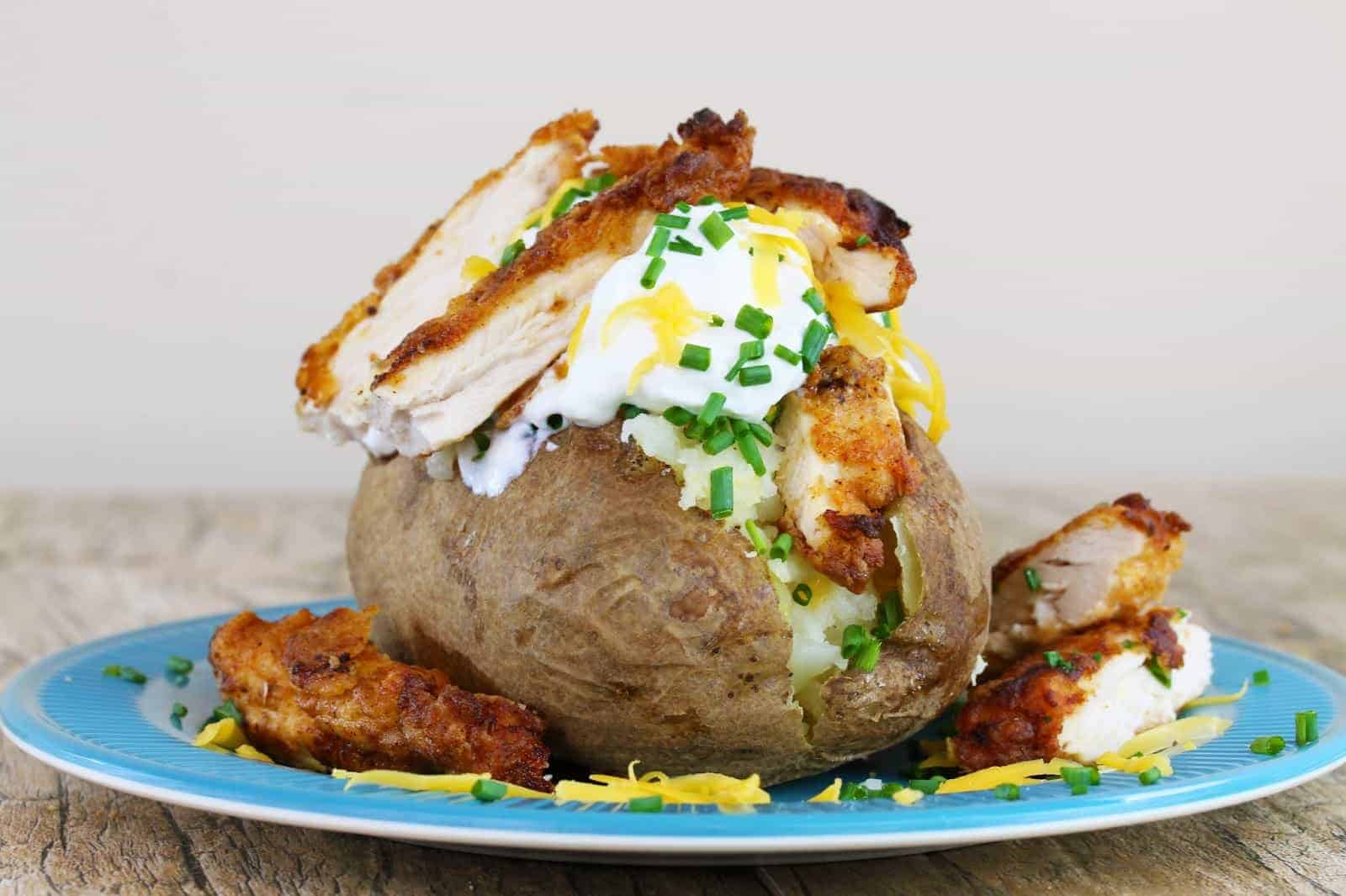 Low view of A baked potato stuffed with sour cream, cheddar cheese and fried chicken, garnished with fresh chives