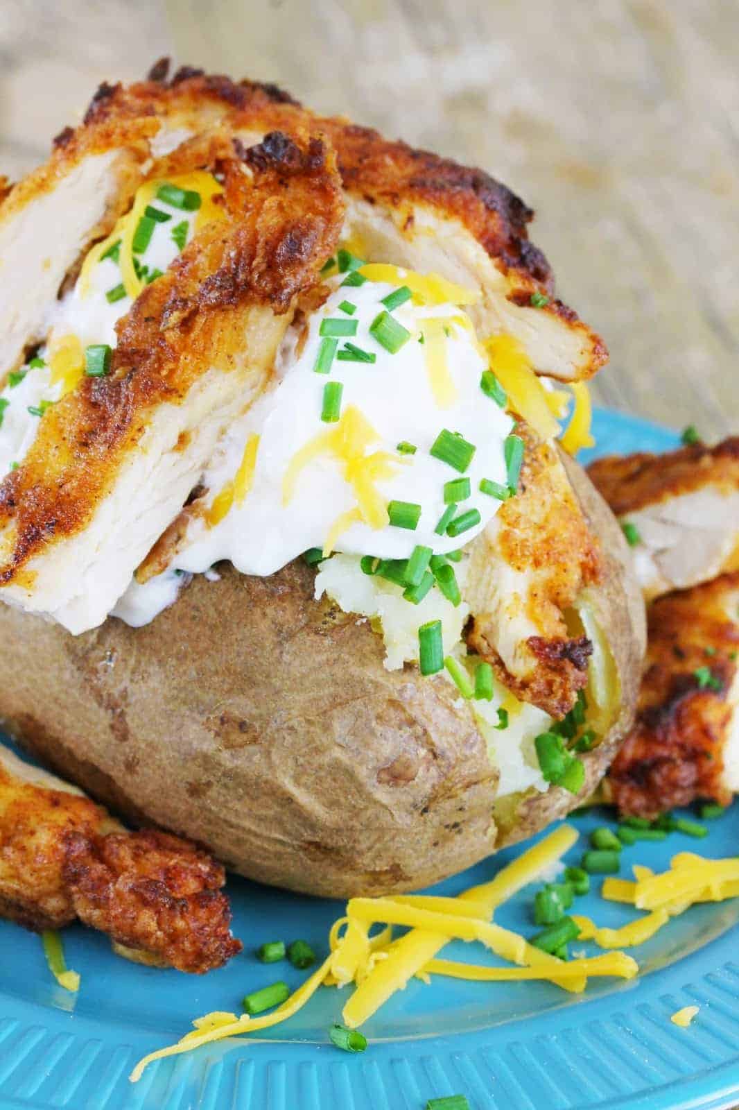 A baked potato stuffed with sour cream, cheddar cheese and fried chicken, garnished with fresh chives