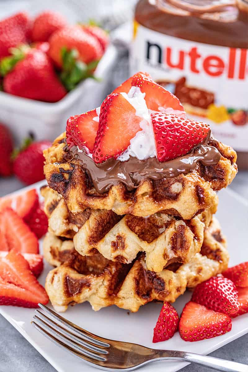 A stack of Liege Waffle topped with nutella, whipped cream and sliced strawberries