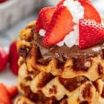 A stack of Liege Waffle topped with nutella, whipped cream and sliced strawberries