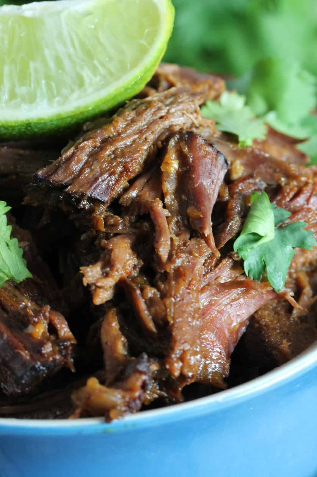 Close up of Easy Slow Cooker Chili-Lime Mexican Shredded Beef in a Crockpot, garnished with cilantro and fresh lime wedges