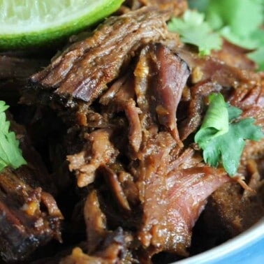 Shredded Beef in a blue bowl topped with a lime slice and parsley.