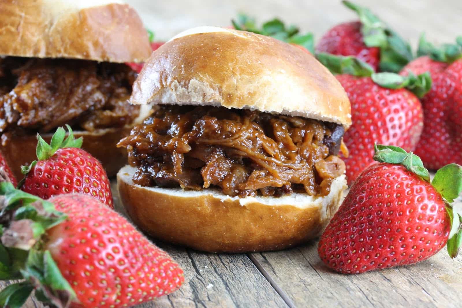 Slow Cooker Strawberry Chipotle Pulled Pork on a bun, surrounded by strawberries