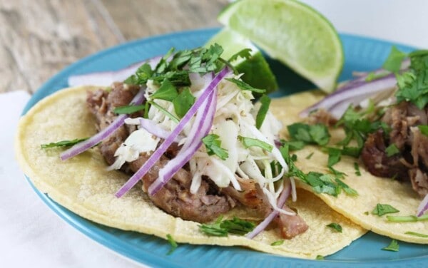 Slow Cooker Mojo Pork Taco topped with slaw, red onion, cilantro and lime wedges