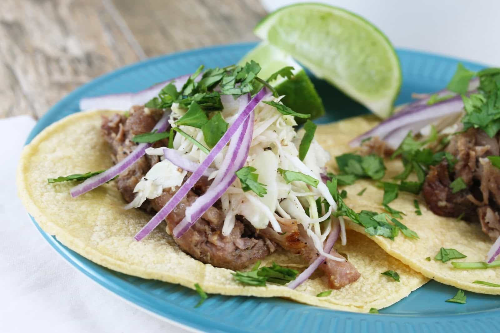 Slow Cooker Mojo Pork Taco topped with slaw, red onion, cilantro and lime wedges
