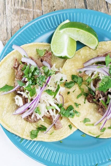 Cuban mojo pork tacos with lime wedges on a blue plate