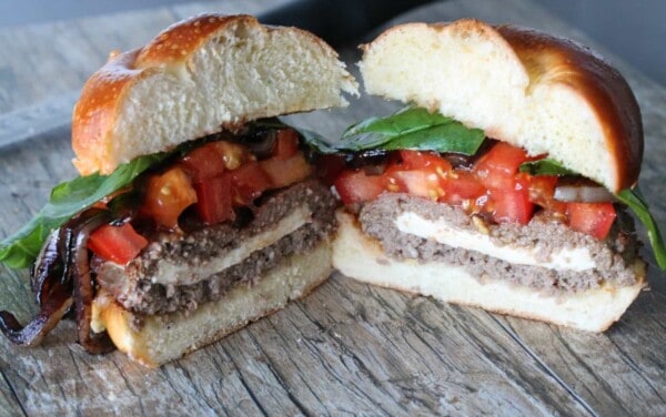 Stuffed Caprese Burger cut in half to show layers of mozzarella, tomatoes, and basil with burger