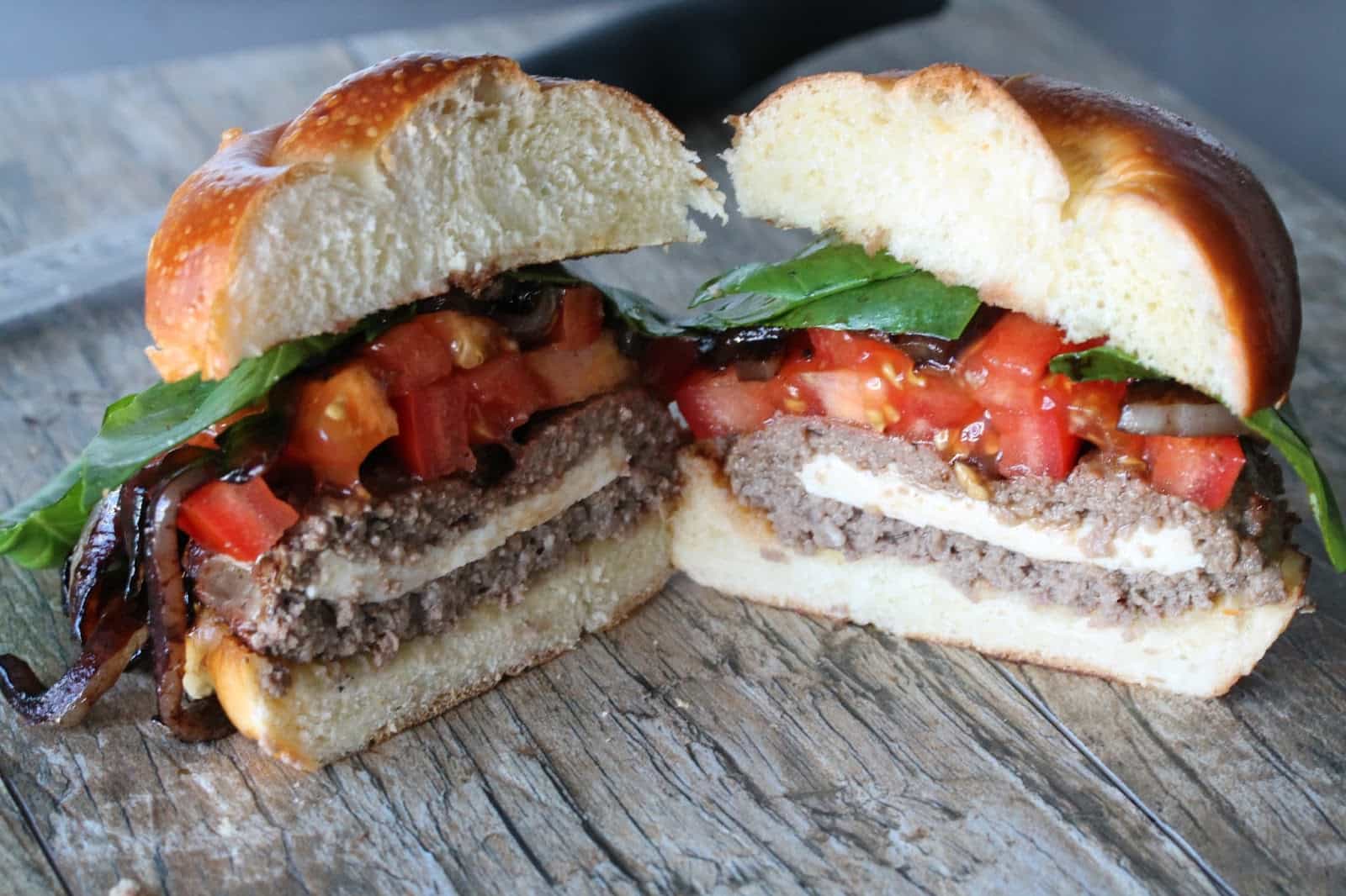 Stuffed Caprese Burger cut in half to show layers of mozzarella, tomatoes, and basil with burger