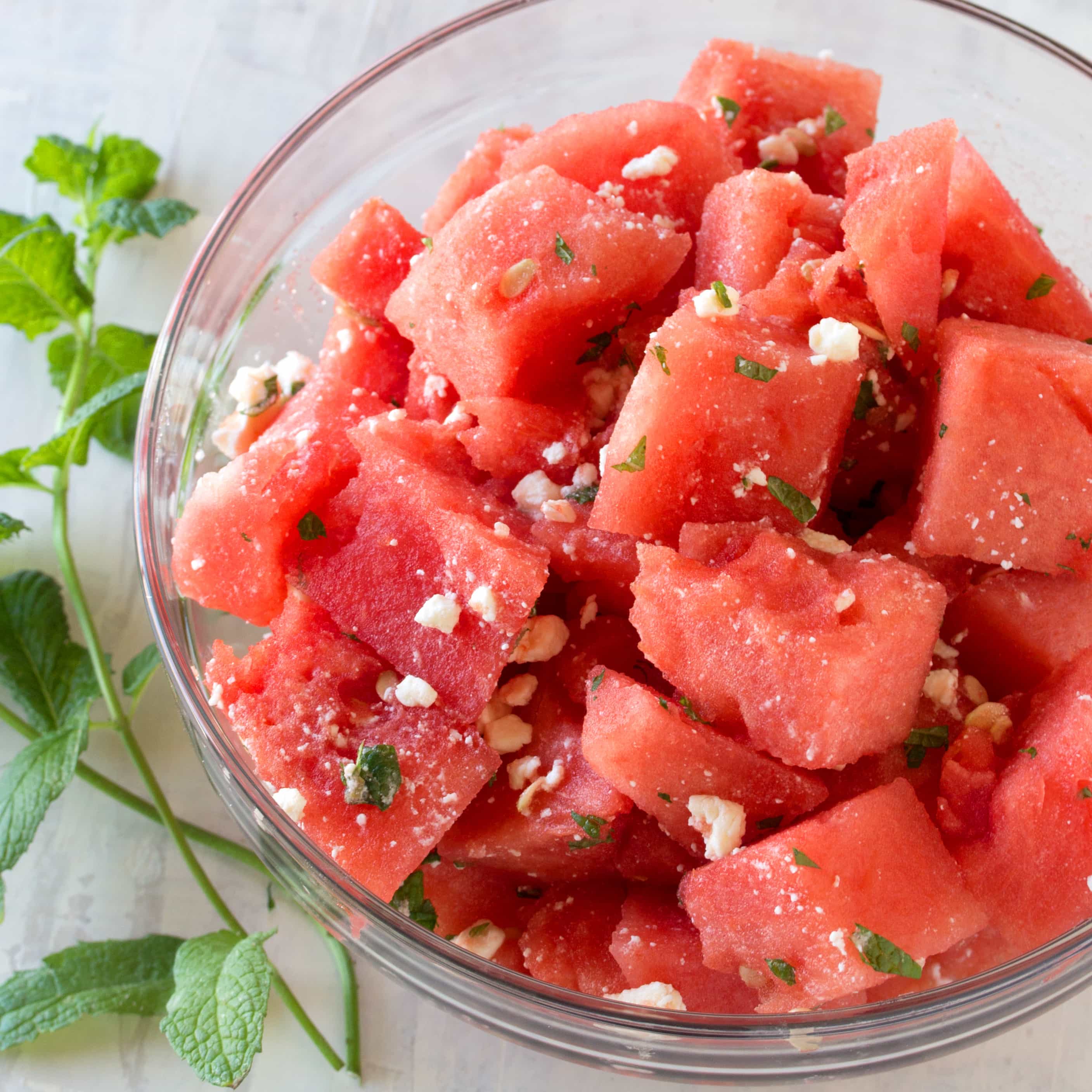 Watermelon Feta Salad served in a glass bowl surrounded by sprigs of fresh mint