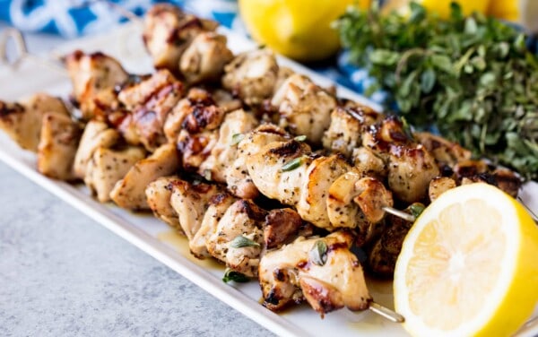 A stack of Grilled Lemon and Herb Chicken Thigh Skewers on a white serving plate with a half lemon.