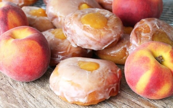 Peach Pie Donuts stacked on a counter with fresh peaches
