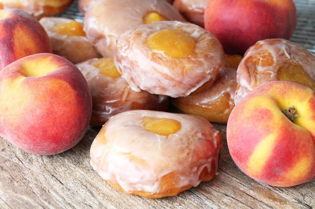 Peach Pie Donuts stacked on a counter with fresh peaches