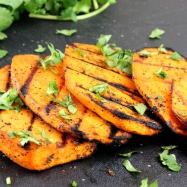 Grilled slices of sweet potatoes on a black cutting board garnished with cilantro